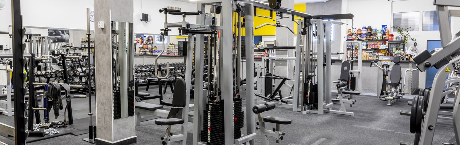 Hlavní sál: kladkové věže, stroje Hammer Strength a v pozadí recepce s barem